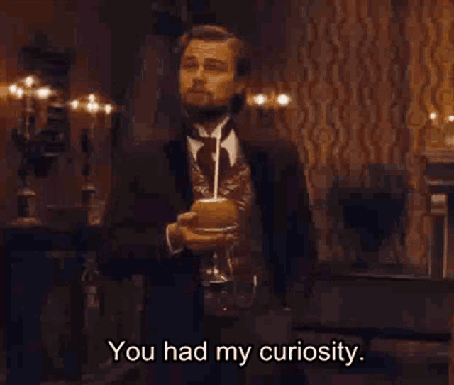 Man in a dark period suit holding a drink with a straw, subtitled 'You had my curiosity'